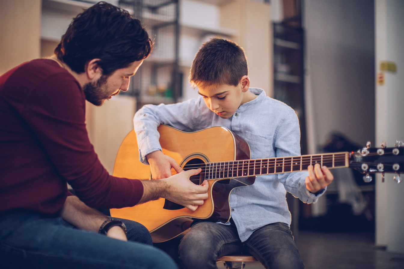 Guitar teacher teaching boy to play acoustic guitar